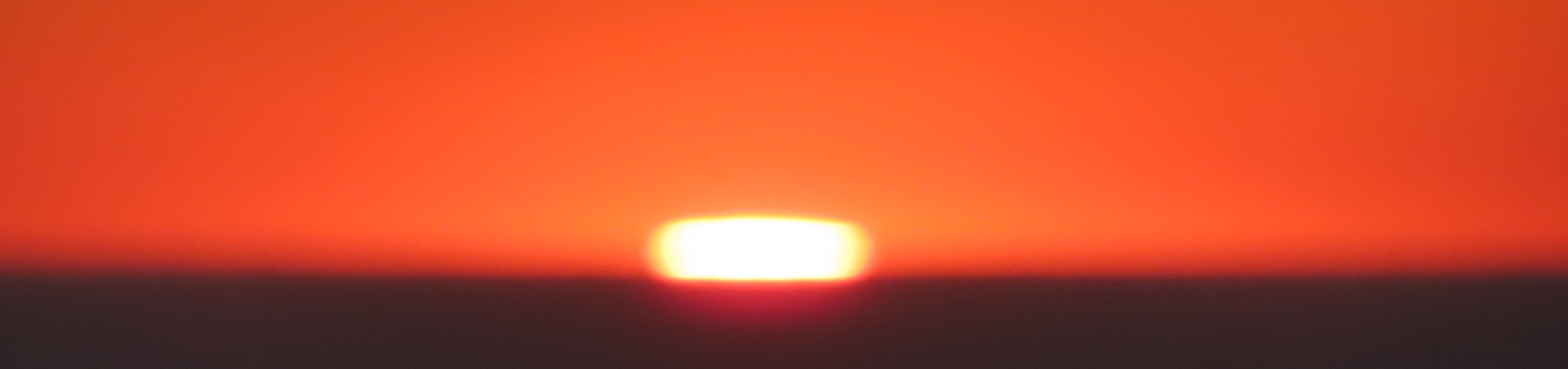 Abstract sunset. A blurry photo depicting a yellow lozenge nestled between a gradient of orange and a fuzzy darkness. Own work, 2023.