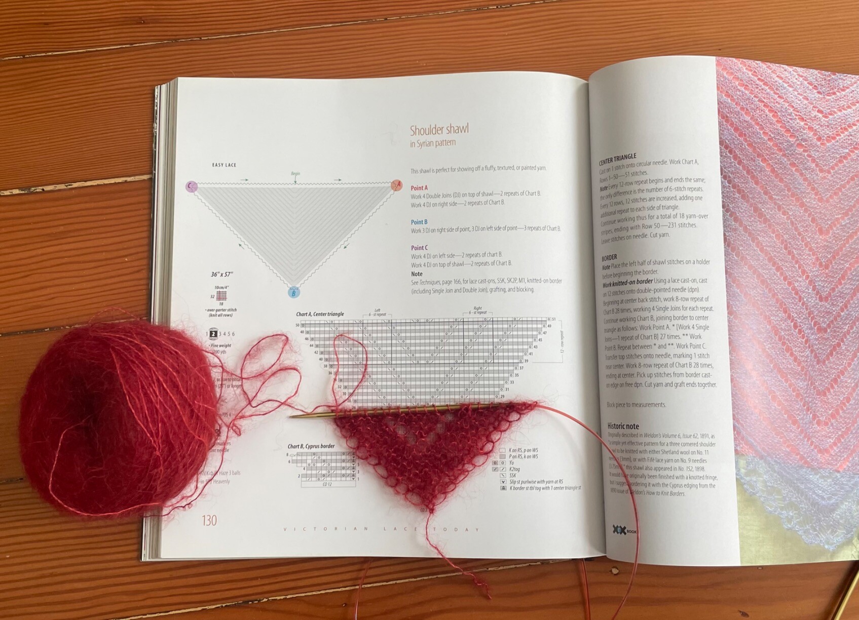 The very beginning of a triangular knit shawl lies on top of an open book with the pattern for that shawl.