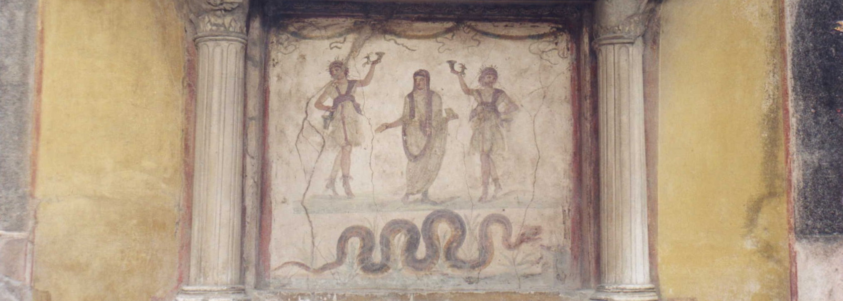Photograph of a first-century Roman Lararium from the House of the Vettii in Pompeii. Photo is an altered version of the creative commons licensed photo found on https://commons.wikimedia.org/wiki/File:Vettii.jpg