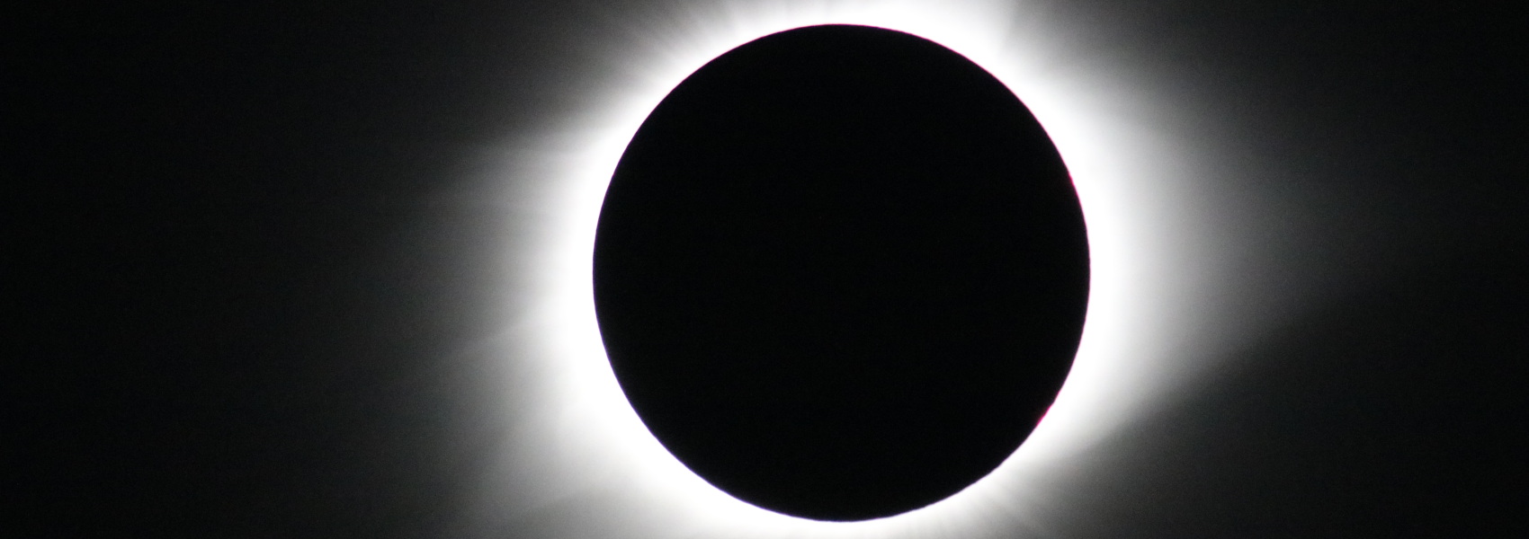 A black hole in a black sky surrounded by a white corona. It is a close crop of a photo of a solar eclipse.