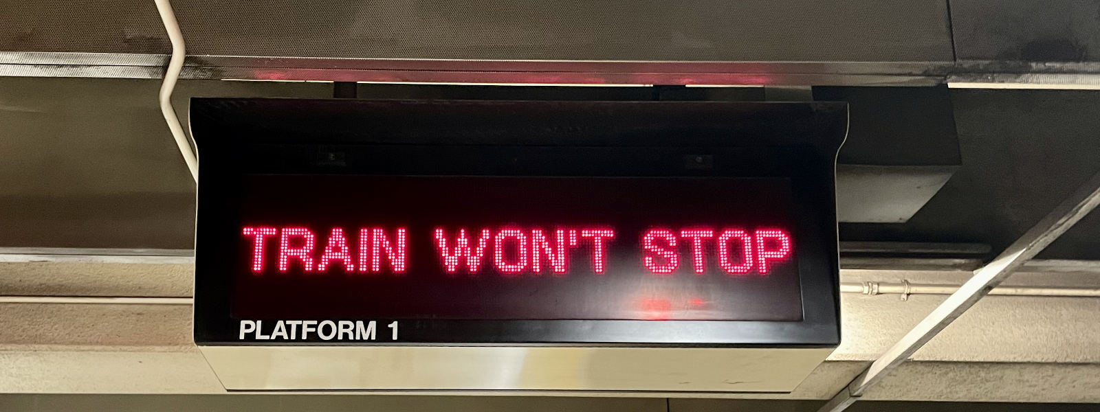 Train won't stop. Photo of a red light display sign above a BART platform that usually displays the destination of the incoming train, in this case it just says TRAIN WON'T STOP. Own work, 2024.